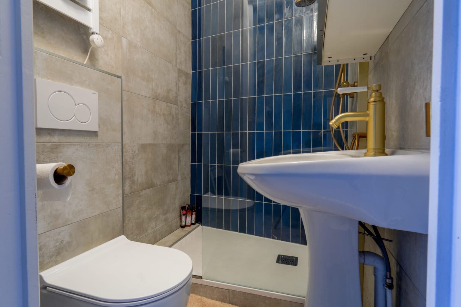 Le Petit Toit Madeleine bathroom with blue faience walls, wall mounted wc, a sink and a golden tap